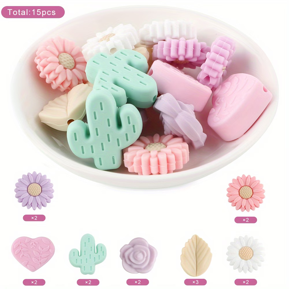A 15-piece assortment of pastel-colored DIY focal beads including mint green cacti, lavender and pink sunflowers, lilac roses, sand-colored leaves, and pink leaf-embossed hearts from Woodland Beads & Co.