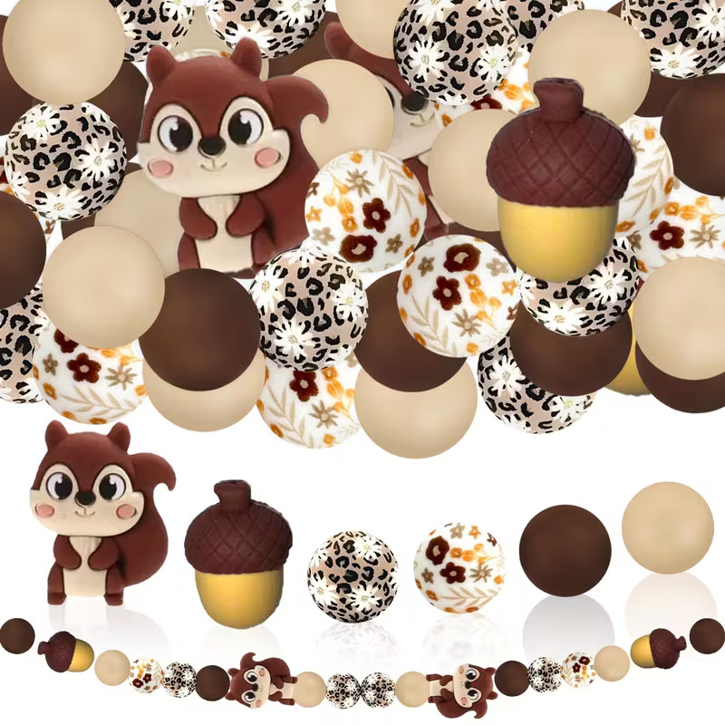 A collection of autumn-themed DIY beads from Woodland Beads & Co featuring squirrel and acorn focal charms, leopard print beads, floral patterned beads, and solid chocolate and beige matte beads.